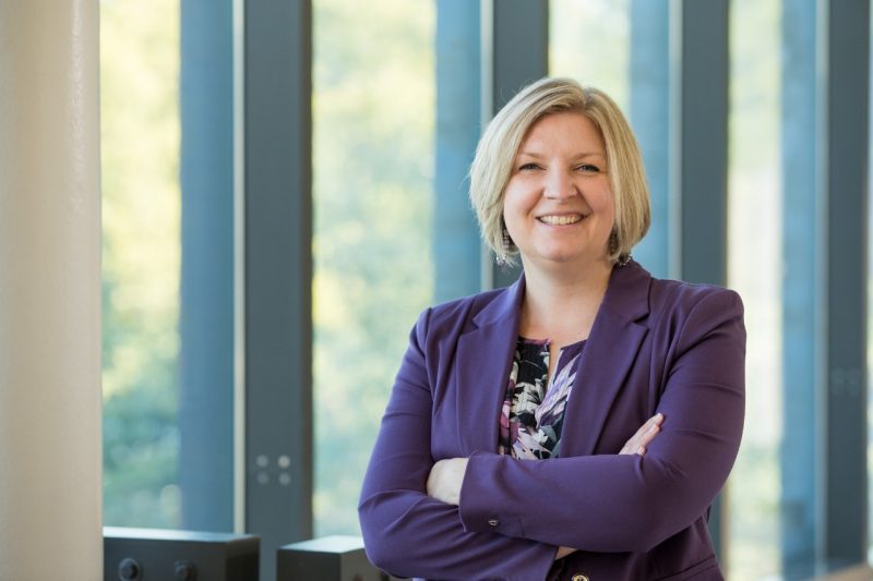 A portrait of Kylene Kehn-Hall in front of large glass windows